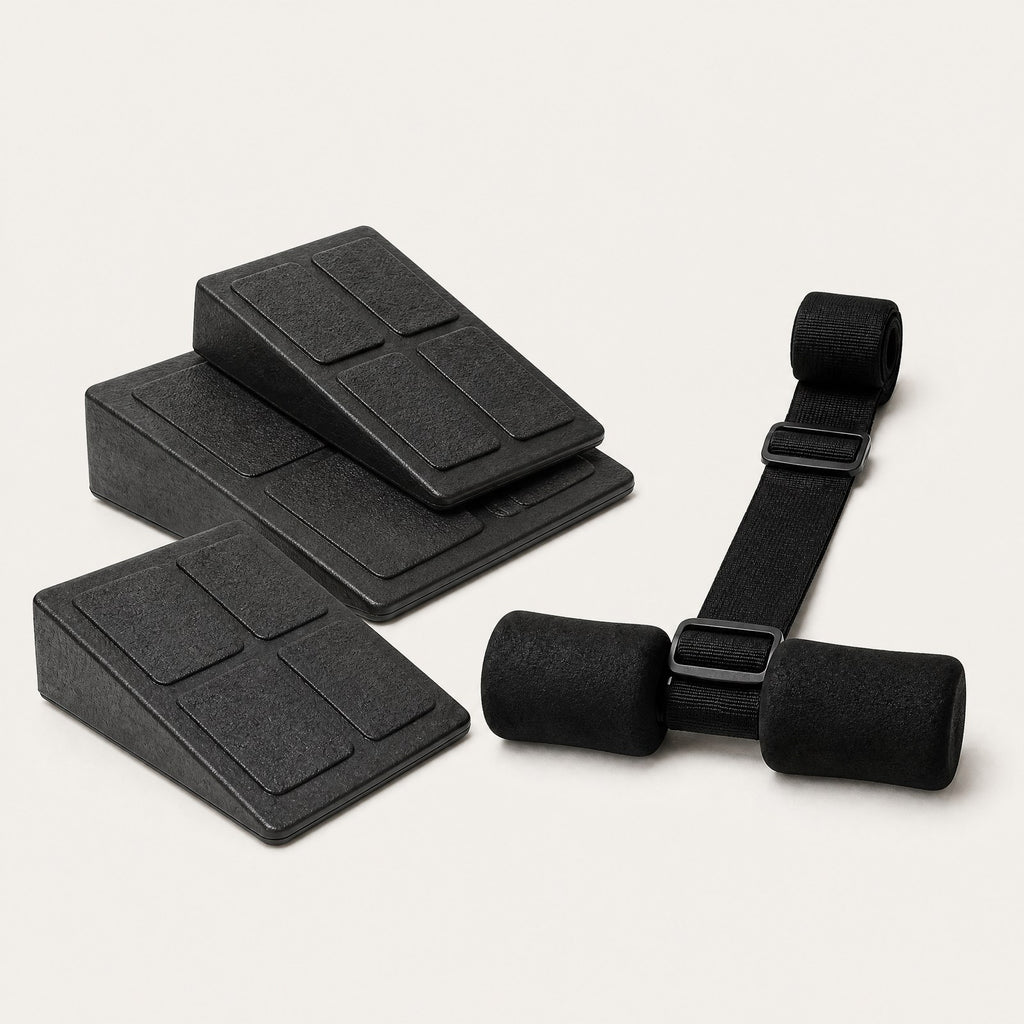 The Longevity Kit: three black rubber squat wedges and the Nordic curl strap with foam ankle rollers